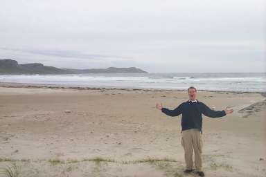 Picture of Armin standing on a beach in a bay, arms stretched out