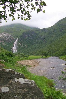 Picture of a glen (valley) with a waterfall at the end and a wide river flowing through it, low clouds above
