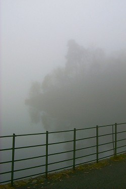 Picture of a rail along a road with an island in a loch in the background just visible in the fog