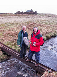 Picture of two people standing on a girder over a burn