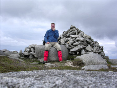 Picture of Armin having lunch sitting on the cairn at the summit of Beinn Bhreac