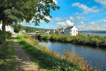 Picture of a canal and houses next to it, a loch and another village in the background