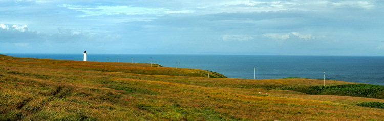 Picture of a panoramic view of a lighthouse at a coast with telephone poles running along the shore
