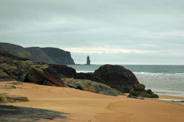 Picture of rocks on a sandy beach and a rock stack in the distance