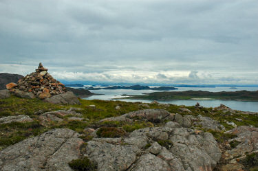 Picture of a cairn on a hill with a view over the sea and islands behind it