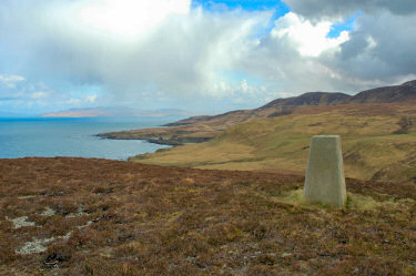 Picture of the summit of a hill with a trig point, coastline in the background
