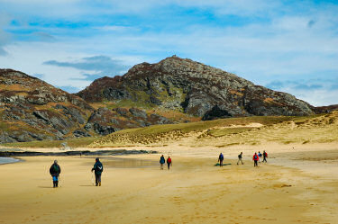 Picture of walkers on a beach, a hill in the background