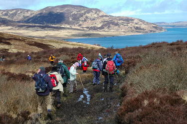 Picture of walkers on a muddy path, a bay in the background