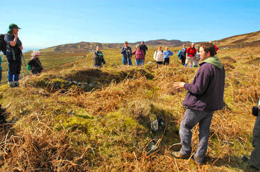 Picture of people standing around the ruins of a chapel, listening to a guide