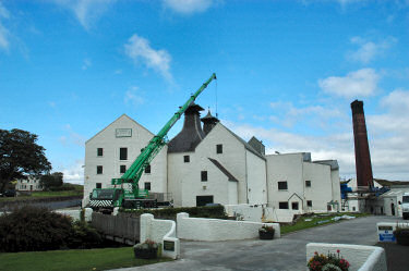 Picture of whitewashed distillery building (Lagavulin, Islay) with a green crane in front of it