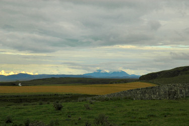 Picture of a view over fields and rolling hills with three small mountains in the distance