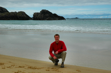 Picture of a person kneeling down on a beach, the sea in the background