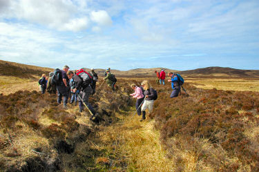 Picture of walkers crossing a ditch with a dried out burn (stream)