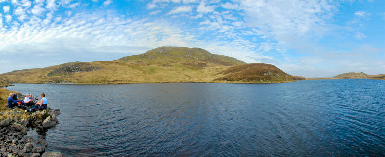 Picture of a group of people sitting next to a loch (lake) under a hill