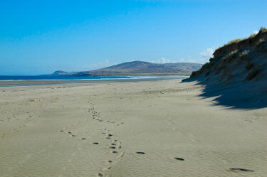 Picture of a beach stretching out in the distance, dunes on the right, hills on the horizon