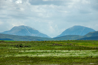 Picture of two distinctively shaped mountains, a field with cotton grass in the foreground