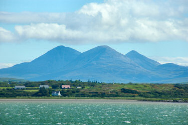 Picture of three large round shaped mountains (The Paps of Jura) seen across a sea loch