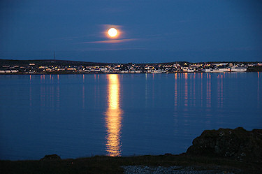 Picture of the moon rising over a coastal village seen across a sea loch