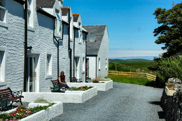 Picture of a young woman sitting on a bench outside a row of cottages