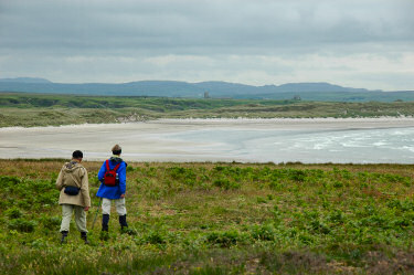 Picture of a couple walking towards a beach across some rough ground