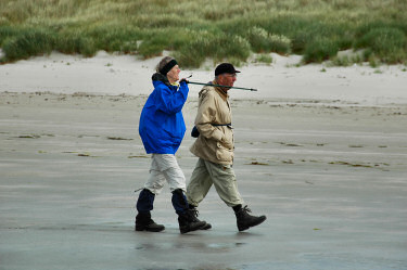 Picture of a couple walking along a beach, the woman pointing with a walking stick