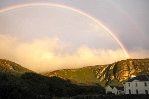 Picture of a rainbow over a white building in front of crags