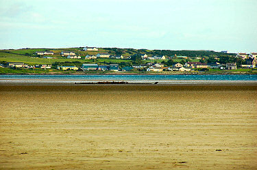 Picture of the remains of wreck in the sand of a sea loch in front of a village