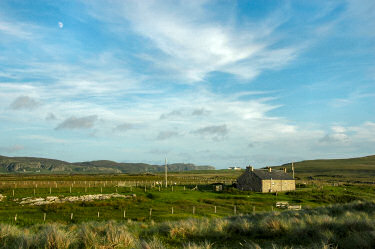 Picture of a stone cottage near a shore, crags in the distance behind it