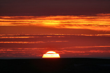 Picture of the sun setting behind low hills