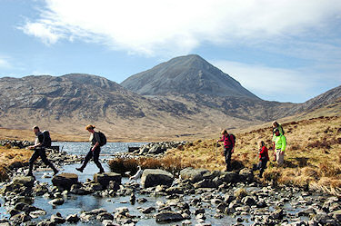Picture of walkers crossing a river under the backdrop of some large mountains